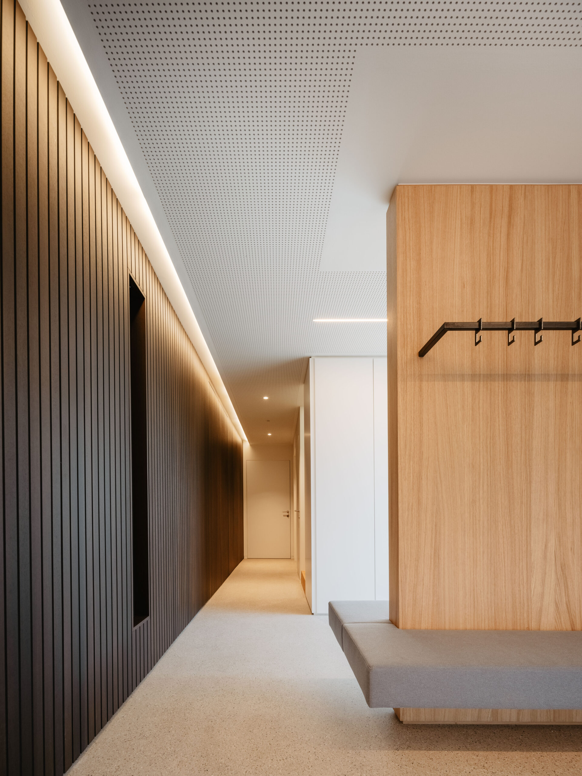 Garderobe aus hellem Holz und Sitzbank aus Stoff, dunkle Wandverkleidung